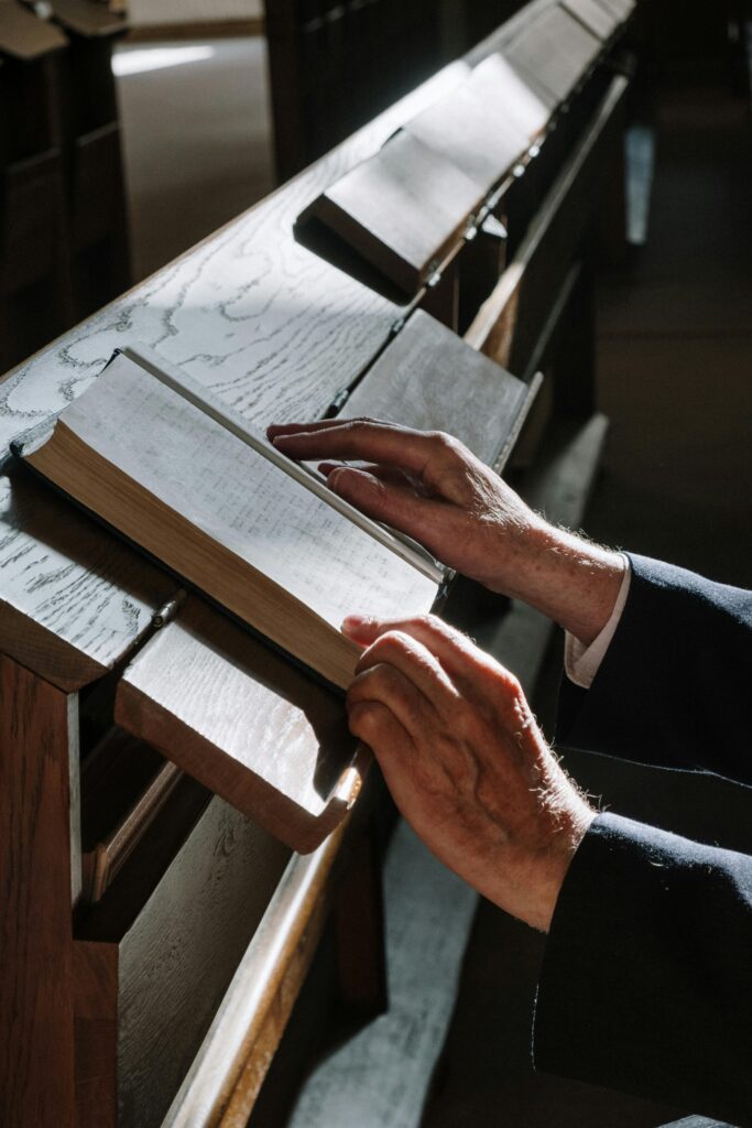 pexels-photo-5974861-5974861 Close-up of hands reading a religious book in a sunlit synagogue, capturing tranquility and devotion.